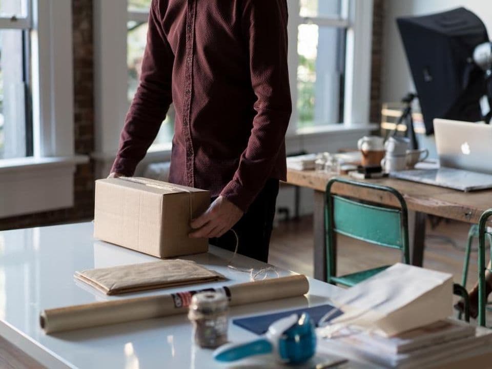 Une personne qui emballe une commande dans un carton, sur un bureau d’atelier